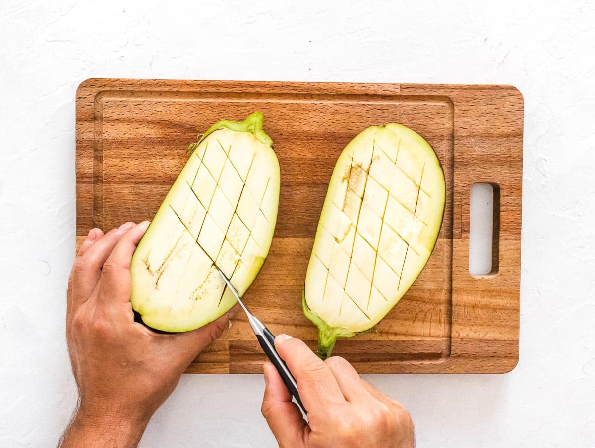 mani e coltello con melanzane tagliate a metà